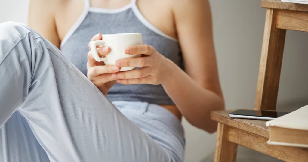 A woman comfortably holding a warm mug of tea, representing relief from IBS and bloating.