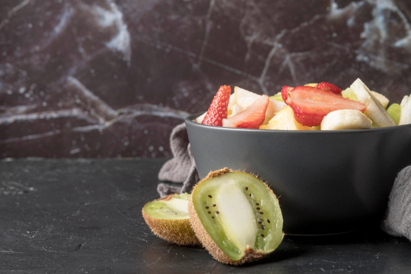 A bowl of fresh, low FODMAP fruits like kiwi and strawberries that do not cause severe IBS bloating.