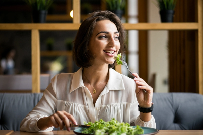 Smiling woman eating a gut-friendly low FODMAP salad at a dining table.